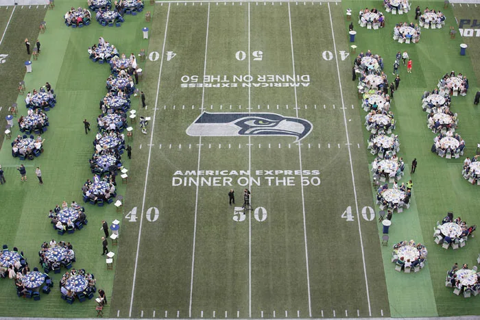 Long dinner tables set across the 50-yard line of a football field